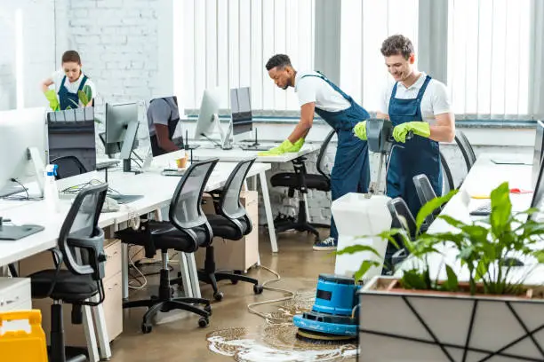 Professional office cleaning services in Cambridge MA showing a janitorial team sanitizing desks and using a floor scrubber machine in a modern open-plan workspace
